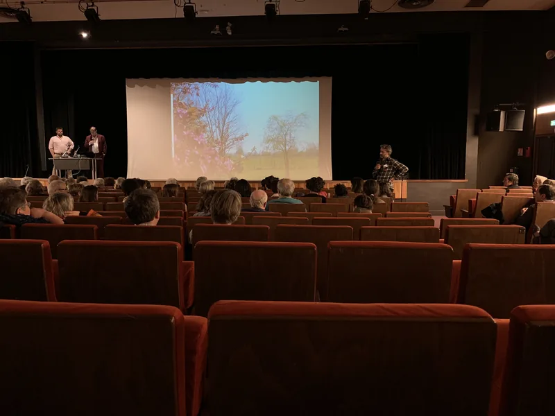 Public assis dans les fauteuils rouges de la salle de spectacle du CCVA, face à une scène avec écran de projection