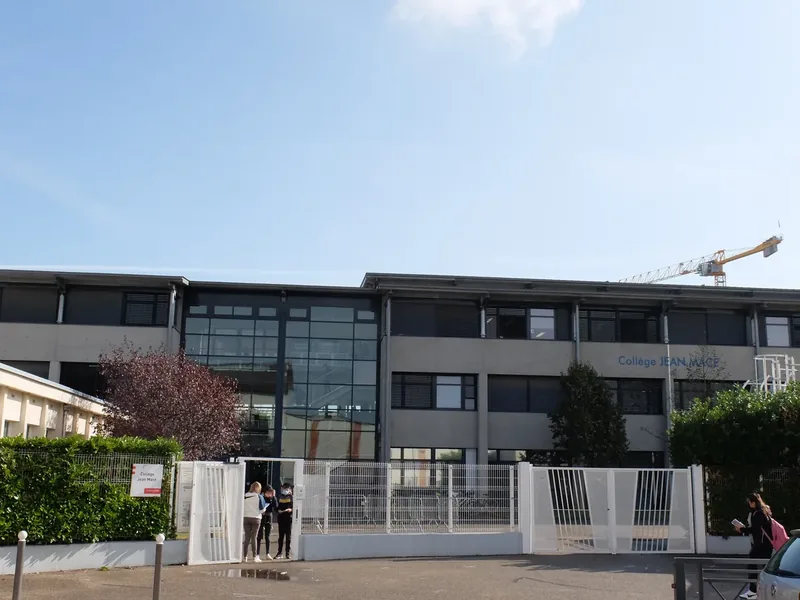Façade vitrée et grilles ouvertes du collège Jean Macé à Villeurbanne, avec des élèves devant l'entrée