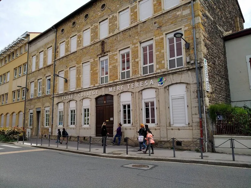 Façade en pierre dorée de l'école et collège Mère Teresa, rue Gervais Bussière à Villeurbanne, avec des familles sur le trottoir