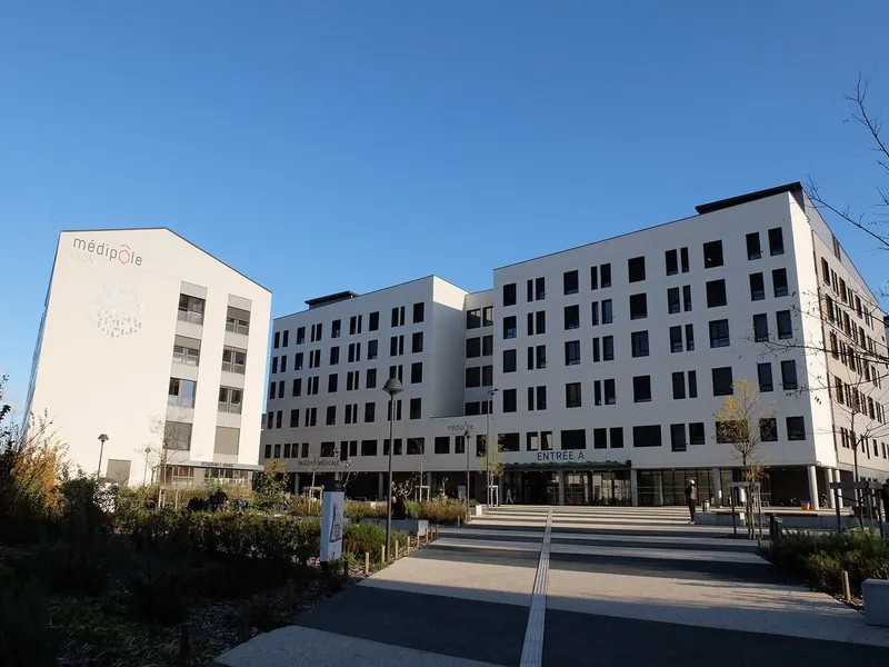 Façade blanche du Médipôle Lyon-Villeurbanne et parvis menant à l'entrée A